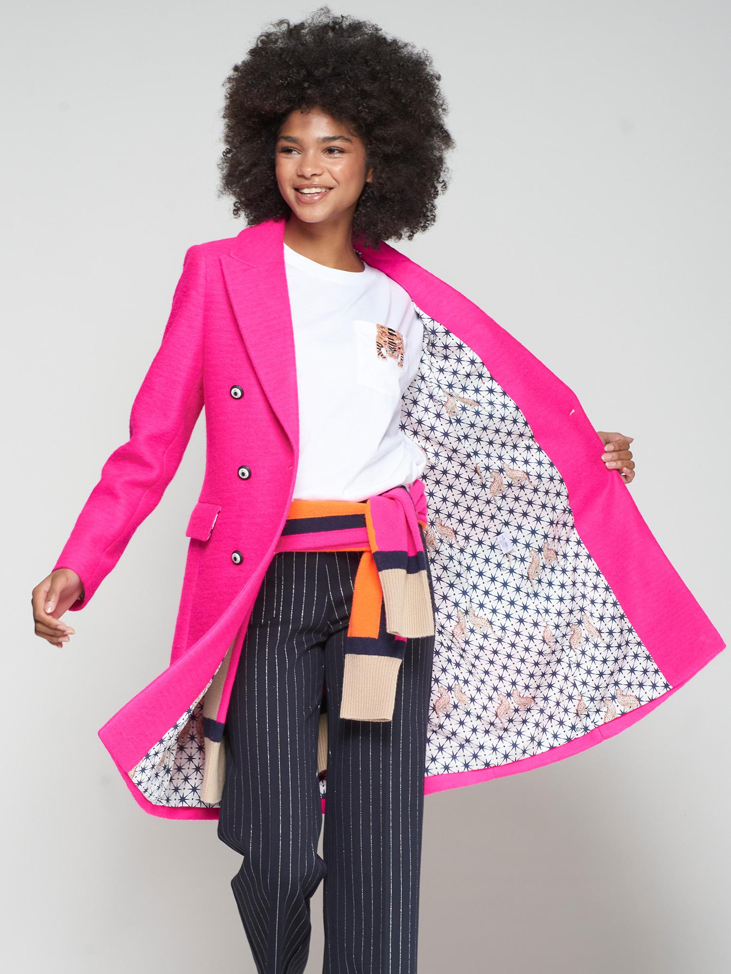 Person wearing a bright pink coat with a patterned lining, standing against a plain background
